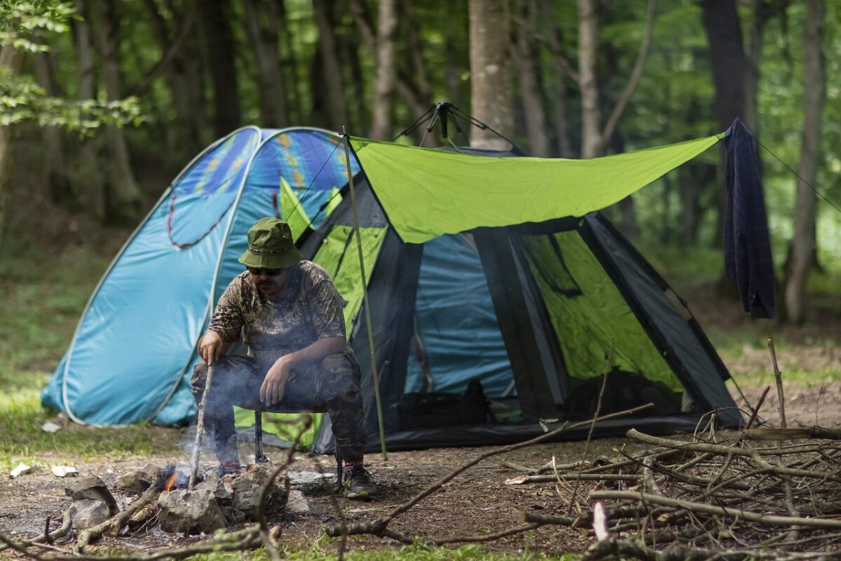 Man after creating his own shade sitting near his tent and burning fire for the food