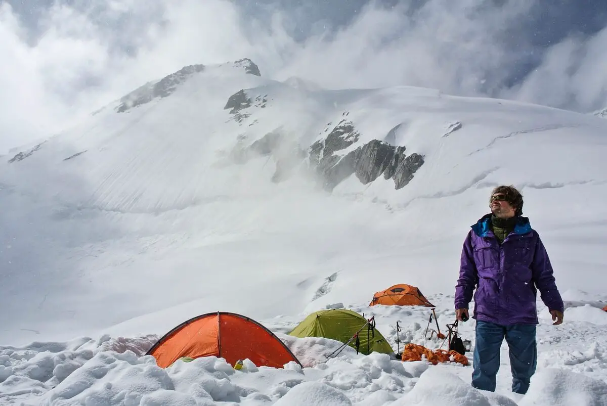 a men standing in the snow while doing  tent camping in winter