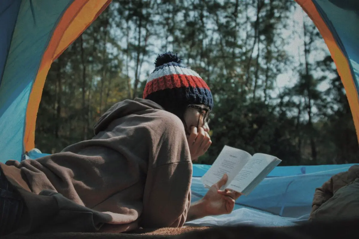 A person reading book inside camping cot in a tent